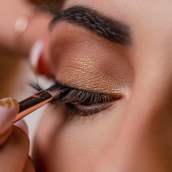 Nahaufnahme eines Auges beim Auftragen von goldfarbenem Lidschatten für ein Abend-Make-up