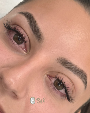 Nahaufnahme eines Gesichts mit betonten Augen und Wimpern, neutralem Hintergrund.