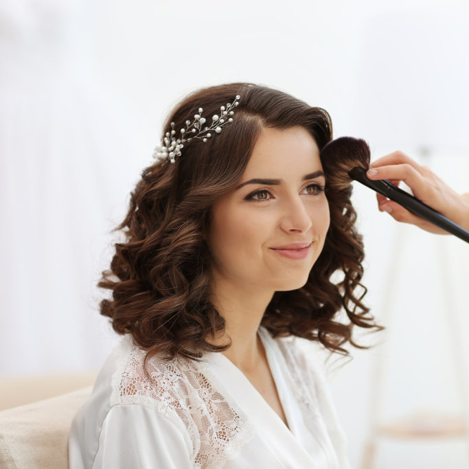 Braut mit lockiger Hochzeitsfrisur während des abschließenden Haarstylings